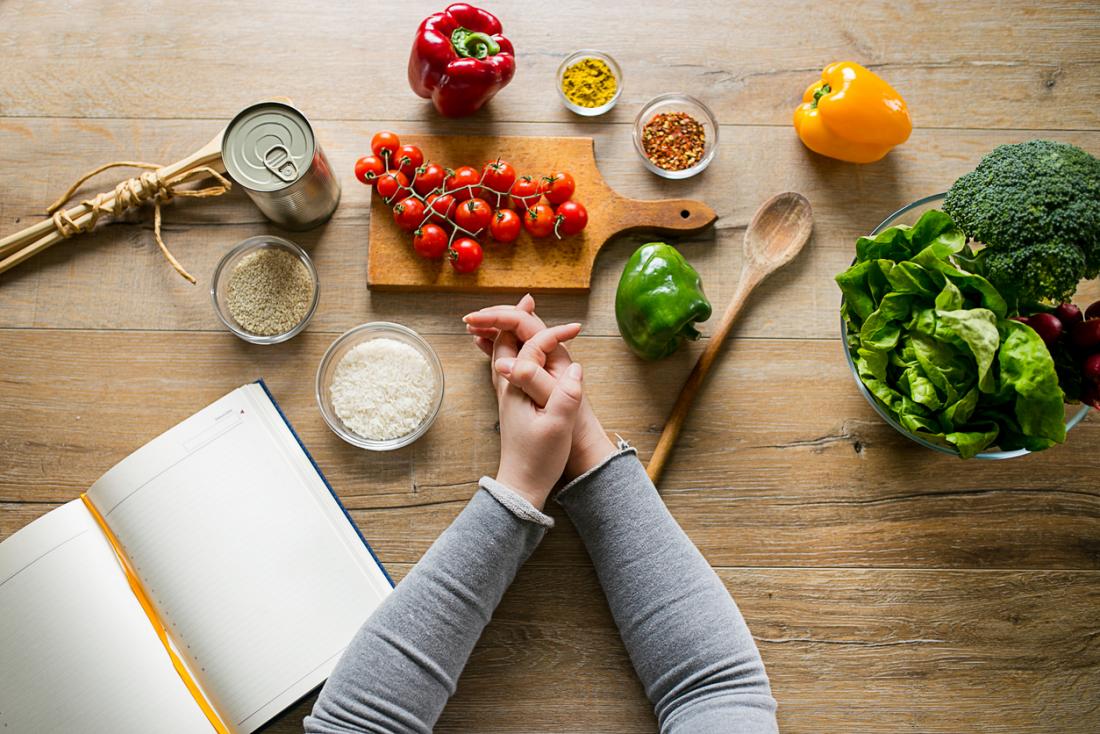 woman leaning on table with various ingredients and a diet planning book